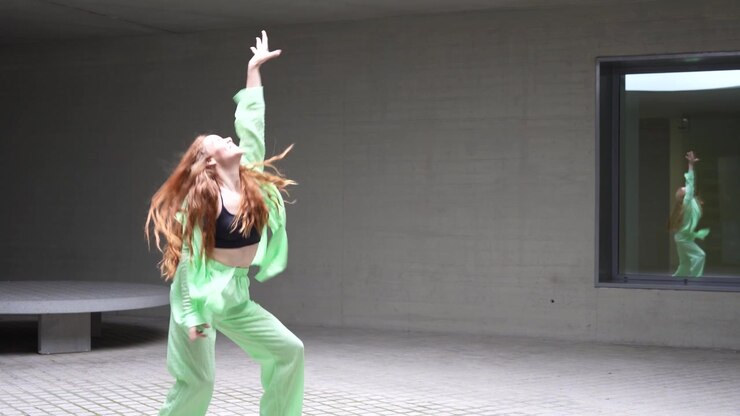 A woman dances in a bright green outfit in a minimalist setting with reflections