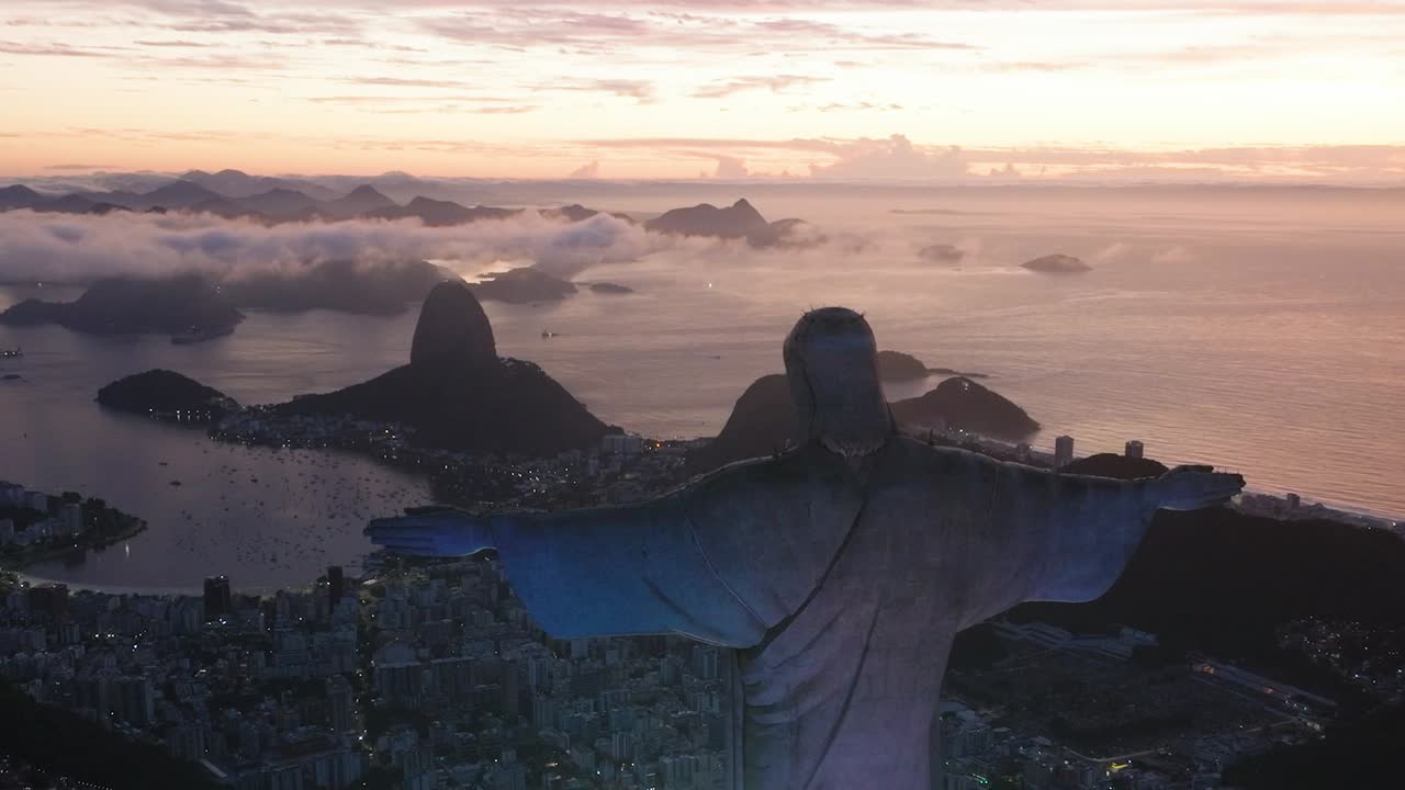 Aerial orbit shot of Christ the Redeemer Statue and Cityscape of Rio de Janeiro at sunset. Aerial wide shot. Cloudscape and coastline with beach at dusk scene. Top down. Peaceful charming atmosphere.