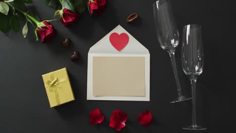 paper heart on envelope and roses with champagne glasses on black background at valentine's day