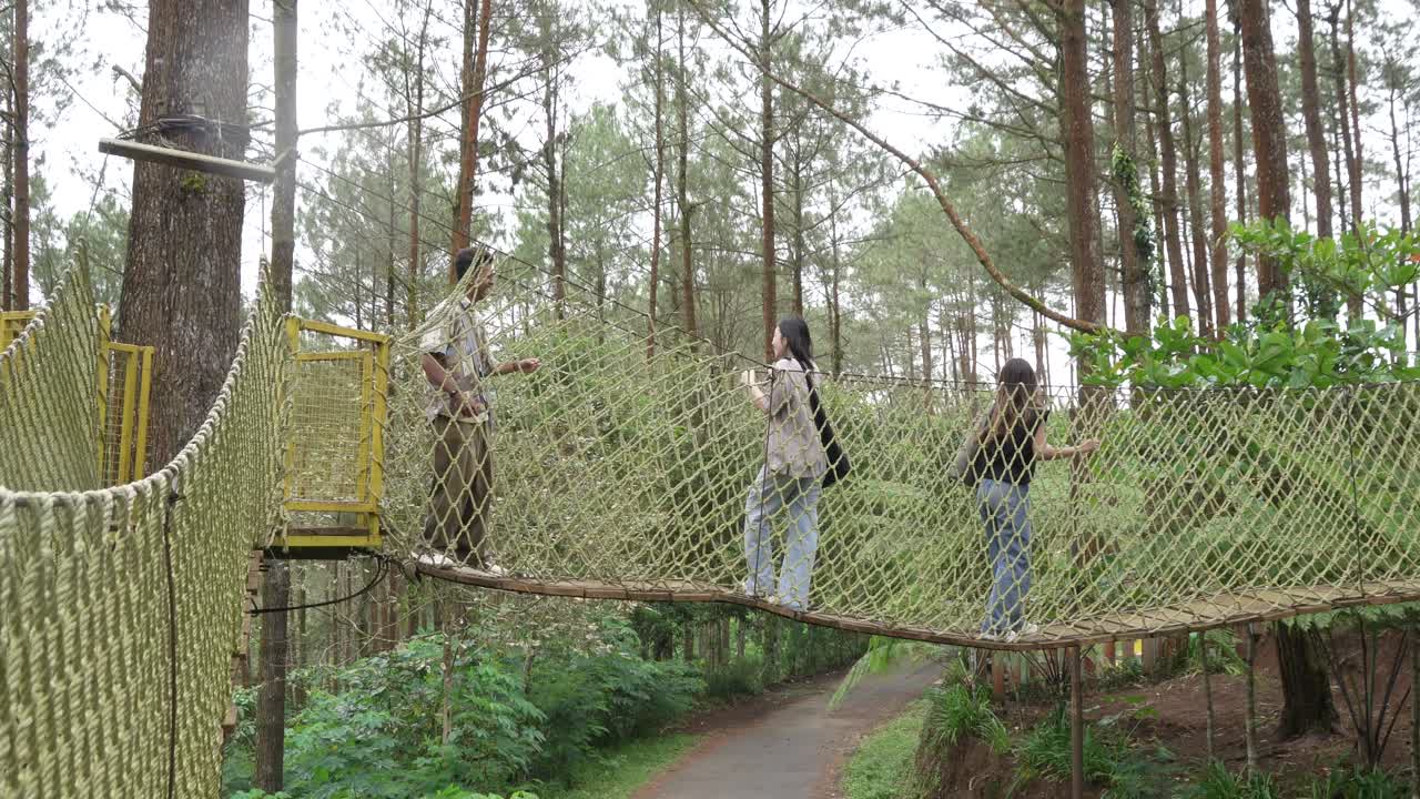 Young Asian Friends Crossing Rope Bridge in Forest Adventure