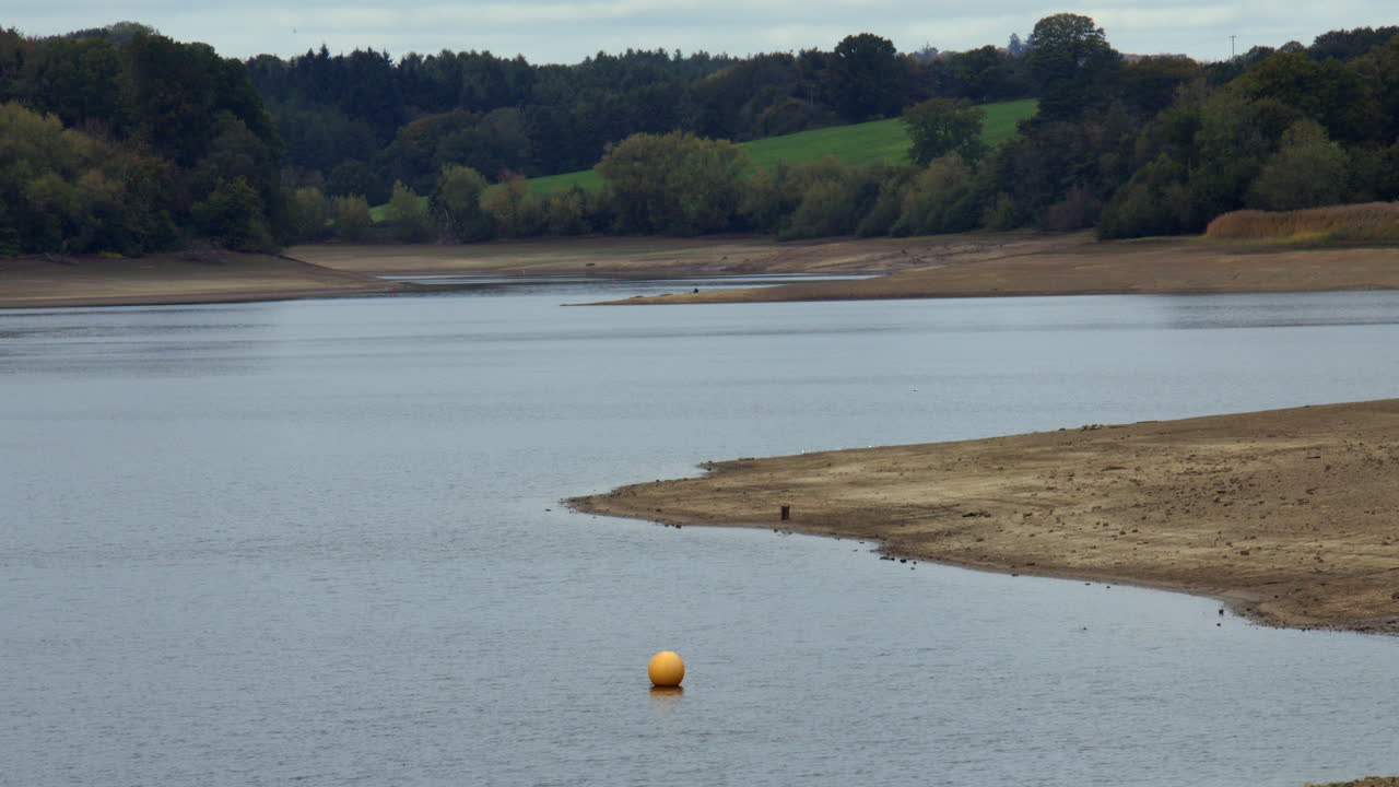 Extra Wide long shot of the tree lined banks of Ardingly reservoir showing low water level