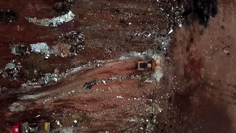 A-straight-down-aerial-view-of-a-bulldozer-pushing-piles-of-trash-over-a-cliff-into-a-landfill