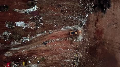 a straight down aerial view of a bulldozer pushing piles of trash over a cliff into a landfill