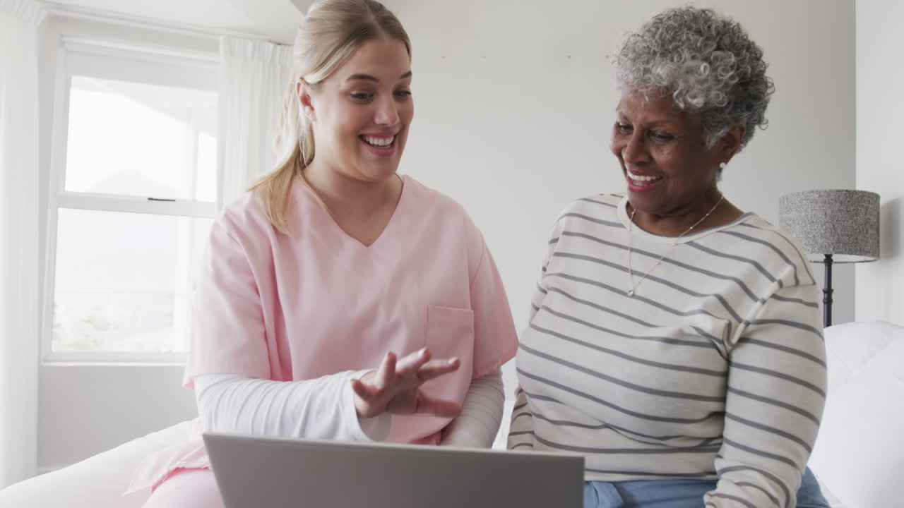 Infermiera caucasica e anziana donna afroamericana che usano un laptop, spazio per il testo, al rallentatore