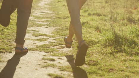 Closeup-of-a-couple's-feet-as-they-run-on-a-path-towards-a-forest