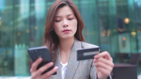 asian happy woman young smiling girl in trendy stylish clothes using credit card with bright colorful shopping bags is using her smart phone while walking in the mall