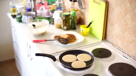 three pancakes are fried in a frying pan, on an electric stove, against the background of the kitchen table.