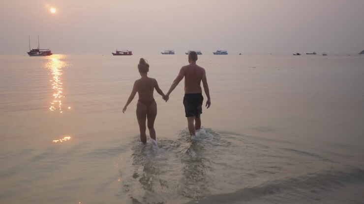 A couple walking hand-in-hand into the ocean at sunset
