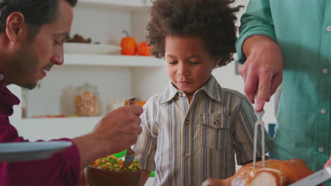 grandfather carves and serves turkey as multi-generation family celebrating thanksgiving with meal
