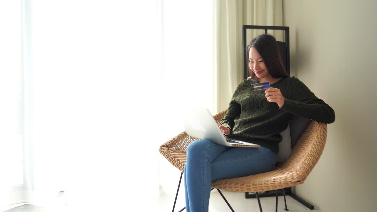 온라인으로 제품을 구매하는 동안 노트북에 신용 카드 번호를 입력하는 매력적인 행복한 아시아 여성