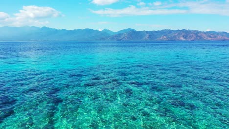 Crystal-emerald-water-of-shallow-azure-lagoon-with-coral-reefs-and-pebbles-underwater,-bright-sky-with-clouds,-Bali