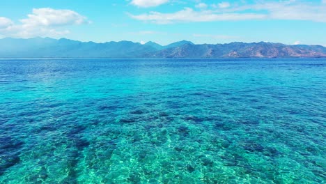 crystal emerald water of shallow azure lagoon with coral reefs and pebbles underwater, bright sky with clouds, bali