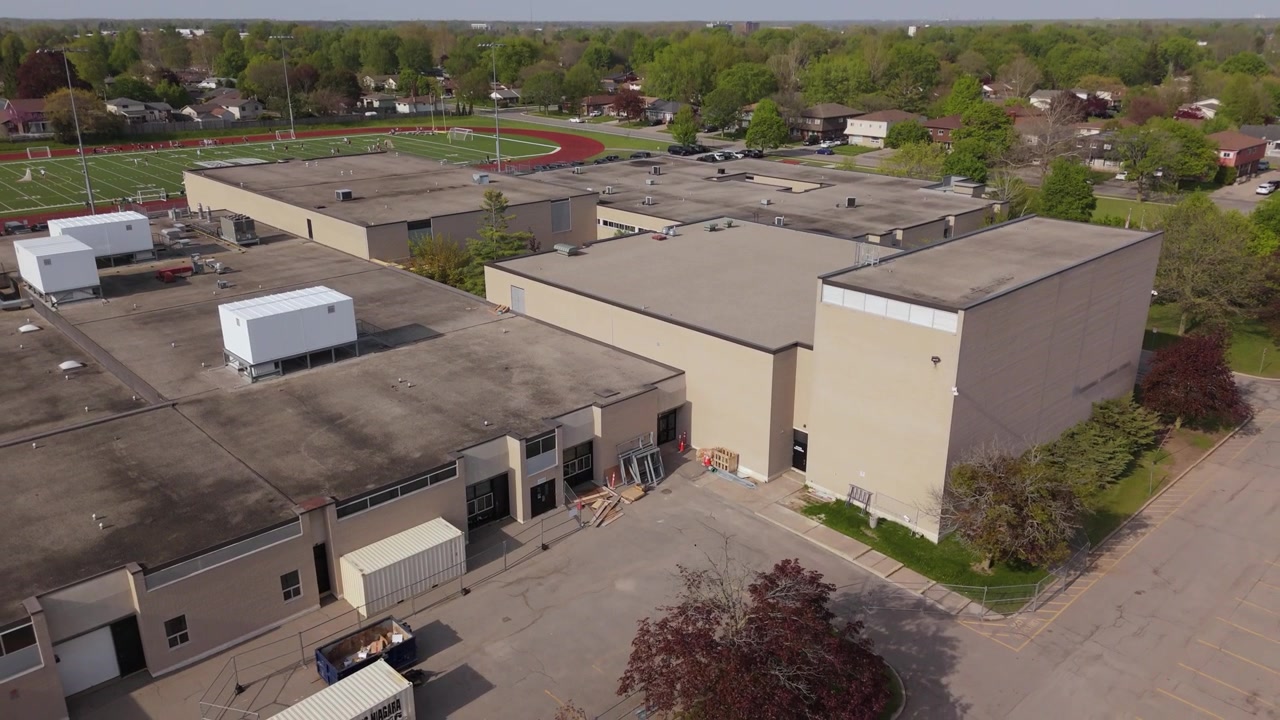 Ripresa drone che si eleva sopra una scuola superiore per rivelare un campo da calcio sullo sfondo.