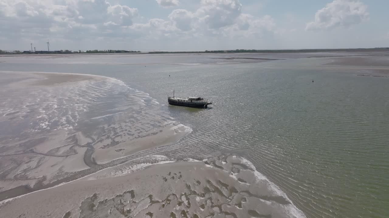 Side profile of a classic boat resting on tidal flats with nearby mud patterns and ripples; daylight, stable framing