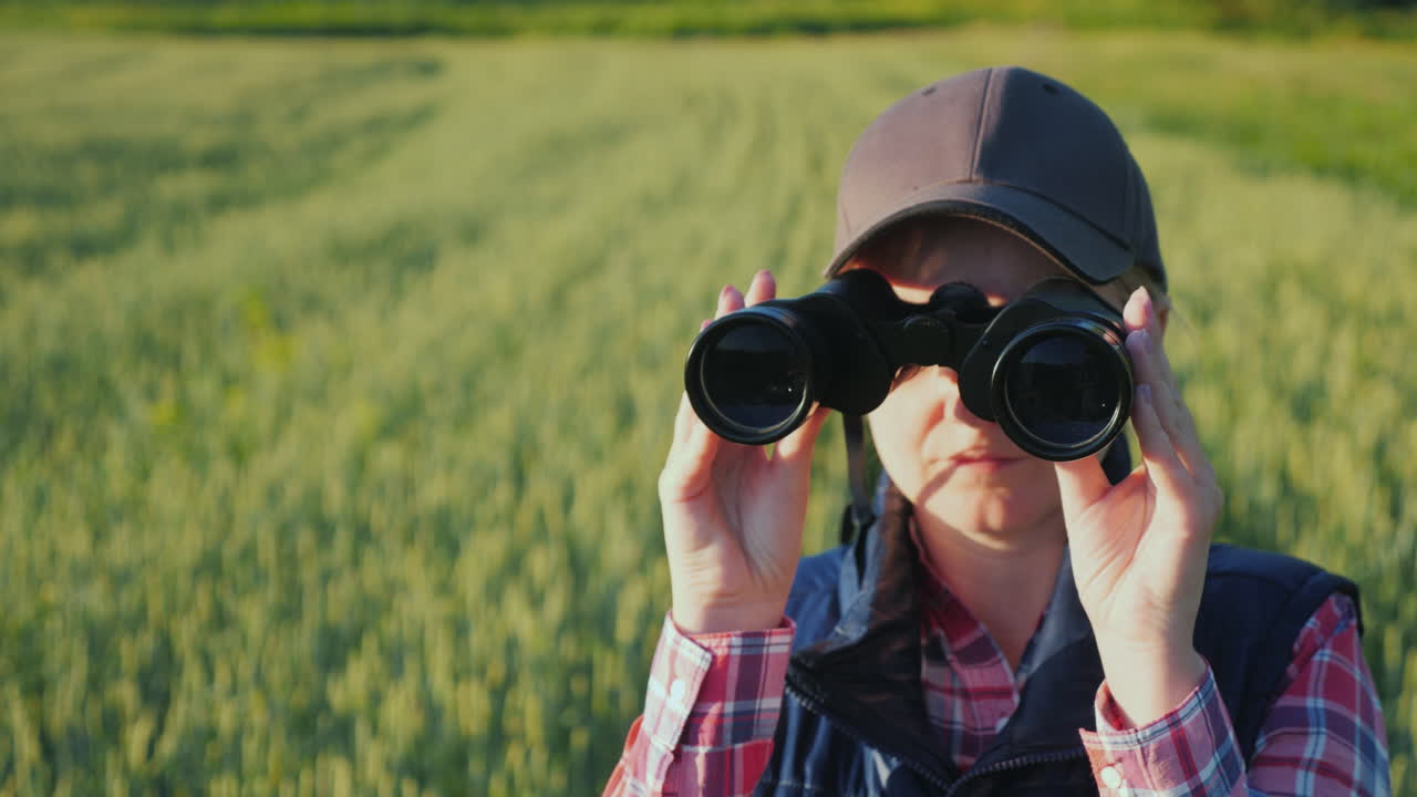 한 여자가 끝없이 펼쳐진 푸른 들판에 서 있는 쌍안경을 들여다본다