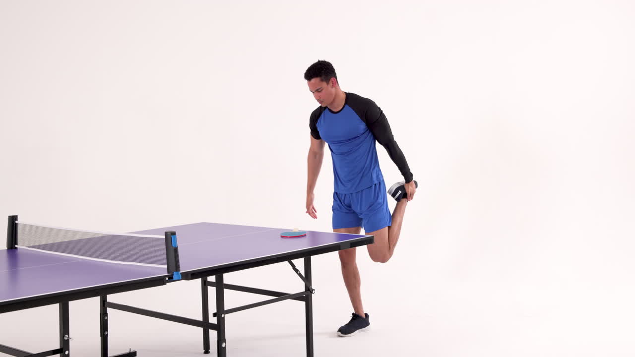 Stretching leg beside table tennis table, man preparing for game in studio