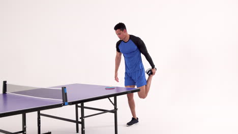 stretching leg beside table tennis table, man preparing for game in studio