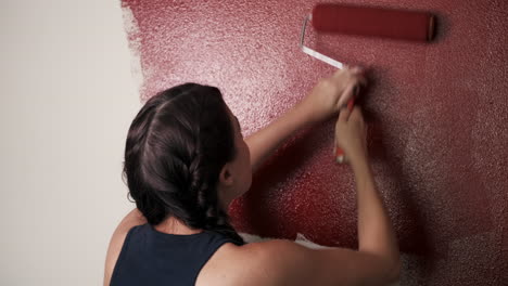 mujer joven pinta pared roja en casa