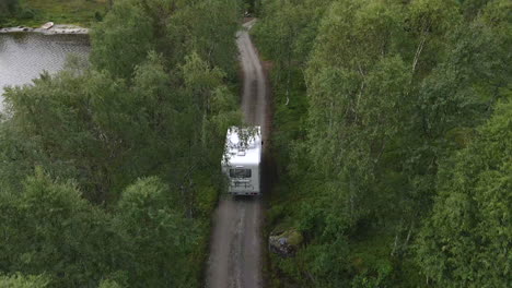 una autocaravana conduciendo por una pequeña carretera en un bosque verde en noruega