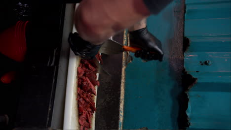 Vertical-slow-motion-of-a-cook-wearing-black-gloves-chopping-slicing-mincing-chorizo-at-a-traditional-mexican-restaurant