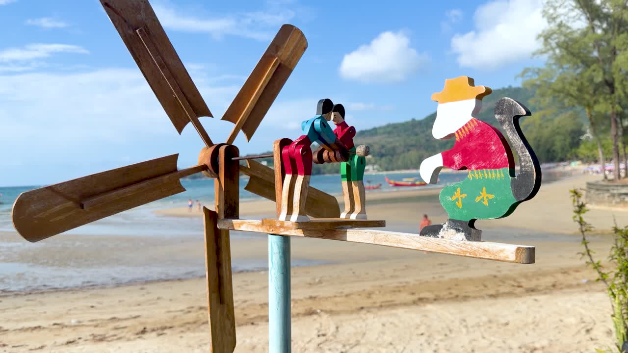 Un colorido molinillo de viento de madera gira en una playa soleada con olas del océano de fondo.
