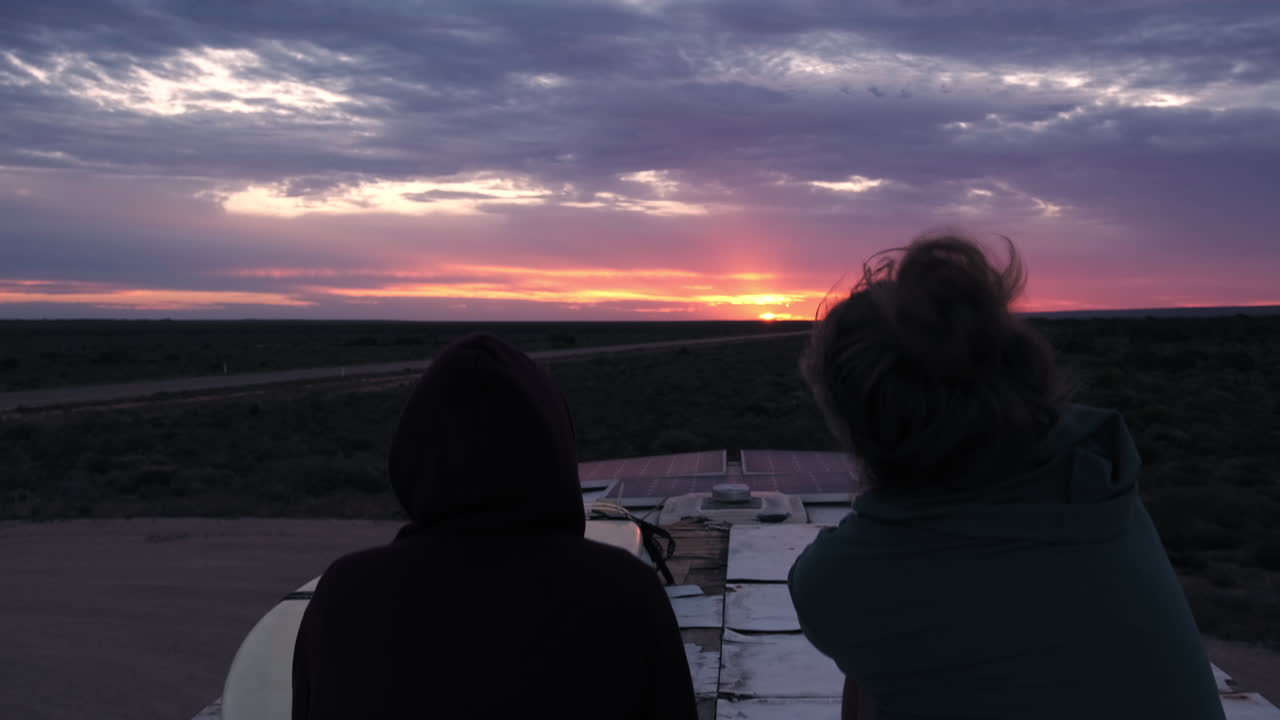 Silhouette of Two peoples sitting on bus and enjoying amazing sunset view in background,ascend shot