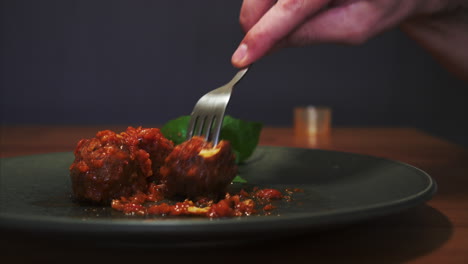 vista lateral de un hombre comiendo albóndigas en salsa de tomate, plato bien presentado y excelente experiencia gastronómica.