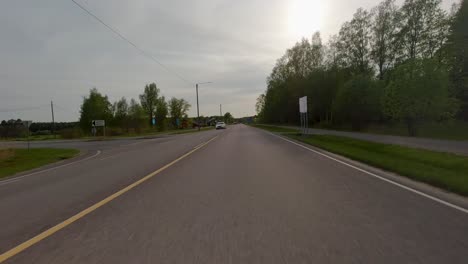 A-long-stretch-of-asphalt-lies-before-me,-framed-by-a-symphony-of-vibrant-green-trees