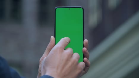 4k close-up of man's hand holding smartphone with green screen on street in city