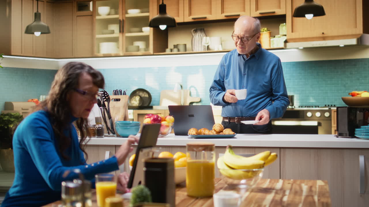 Elderly male adult browsing online on laptop in rustic kitchen space