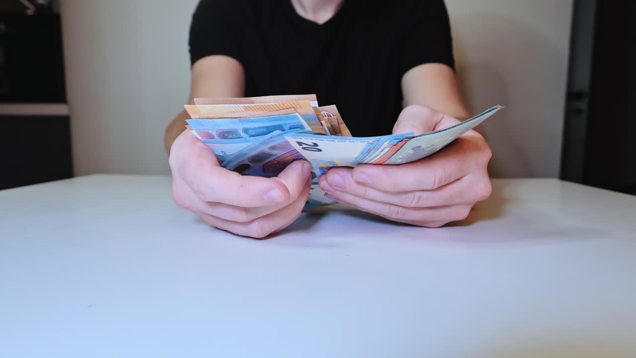 Slow motion shot of young man counting euro cash at table with gradual zoom out