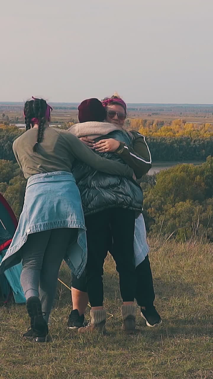 happy tipsy girls hug and spin in dance near blue tent and burning bonfire on sunny autumn day slow motion