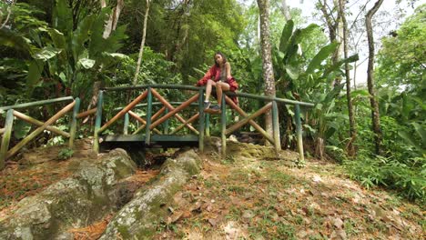 Chica-Elegante-Con-Chaqueta-Roja-Sentada-En-Un-Puente-De-Madera-En-Un-Parque