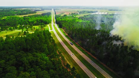 semi-tanker truck drives along a highway in rural georgia, passing by a dense forest where smoke and flames from a wildfire are rising dangerously close to the road.