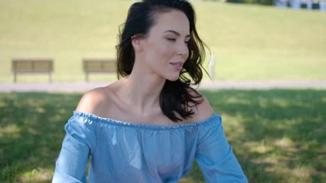 Portrait-of-attractive-brunette-woman-in-blue-dress-sitting-in-a-park