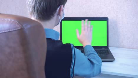 a man greets his colleagues by video calling on a laptop and reminds him to put on a protective face mask, a green monitor screen