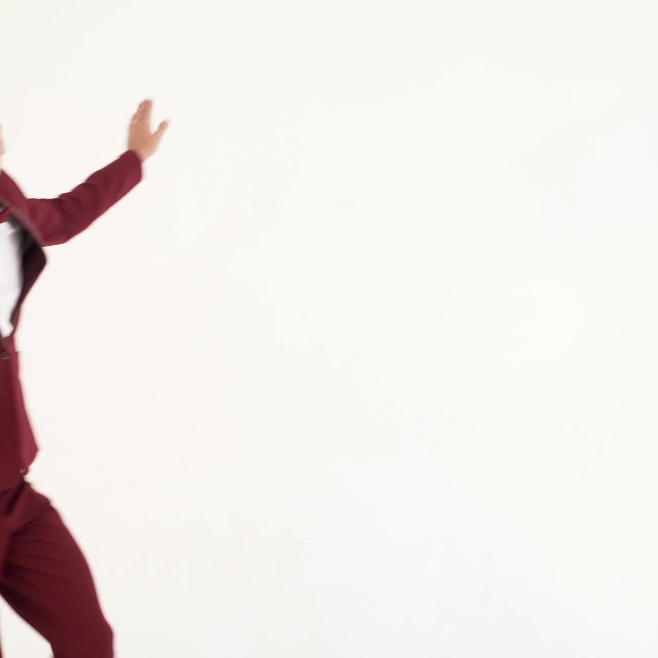 fun showman in red suit is waving his arms and spinning around himself on a white background in the studio