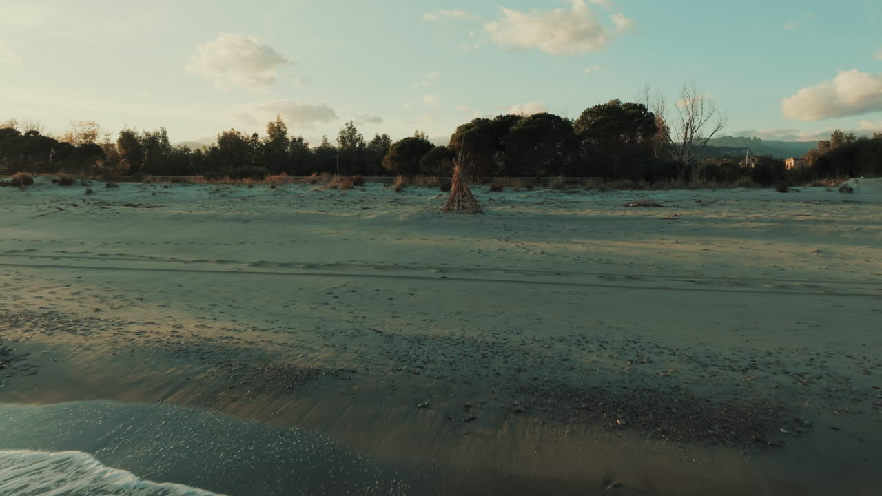 Capanna di canne su spiaggia sabbiosa al tramonto vicino a un oceano calmo