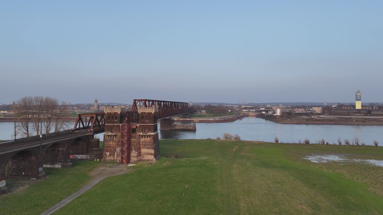 Dron circulando alrededor de la antigua torre del puente con el puente ferroviario, la cuenca del Rin y el horizonte de Duisburg al atardecer.