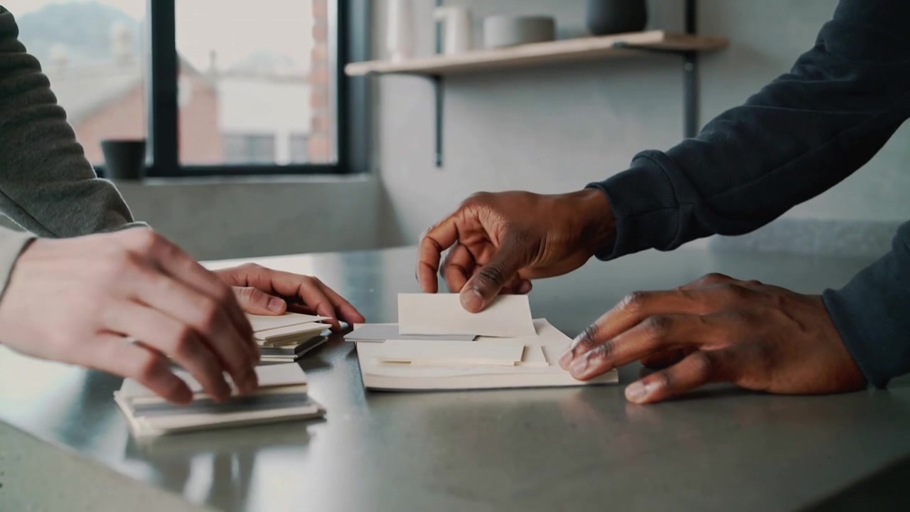 Reaching central stacks, two adults' hands sorting white envelopes on home counter to organize mail