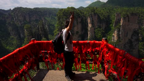 hombre feliz haciendo un signo v disfruta del paisaje cárstico desde un punto de vista con cintas rojas en yuanjiajie, china