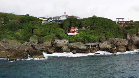 Cinematic-aerial-dolly-out-shot-away-from-sea-god-temple-at-black-dwarf-cave-overlooking-the-whole-islet-against-diffused-horizon-in-Xiaoliuqiu-Lambai-Island,-Pingtung-county,-Taiwan