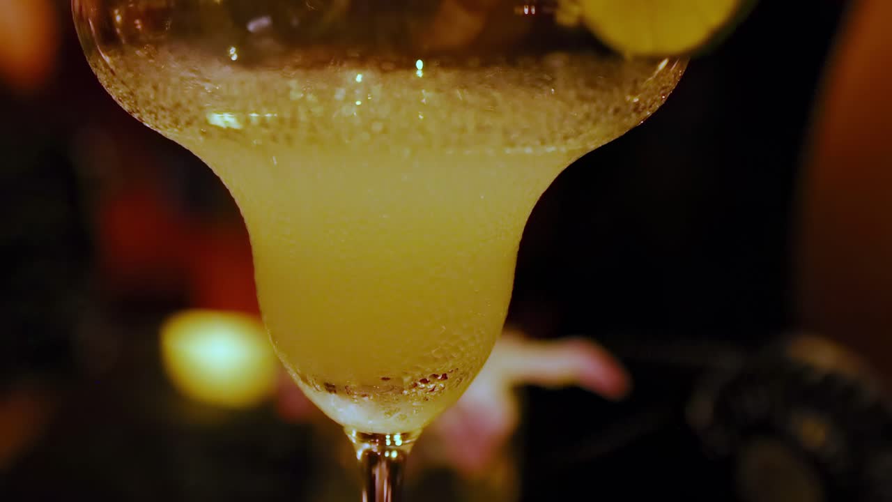 Close-up of cucumber-garnished cocktails with a dimly lit bar ambiance, highlighting the drink's texture and presentation.