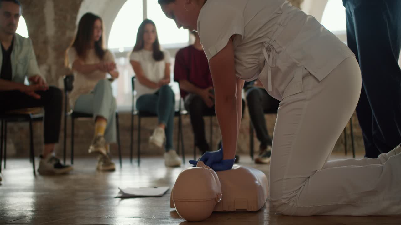 fotografía de primer plano: una doctora en uniforme blanco lleva a cabo una formación médica práctica presionando sus manos sobre el pecho de un maniquí médico para el público, que la escucha