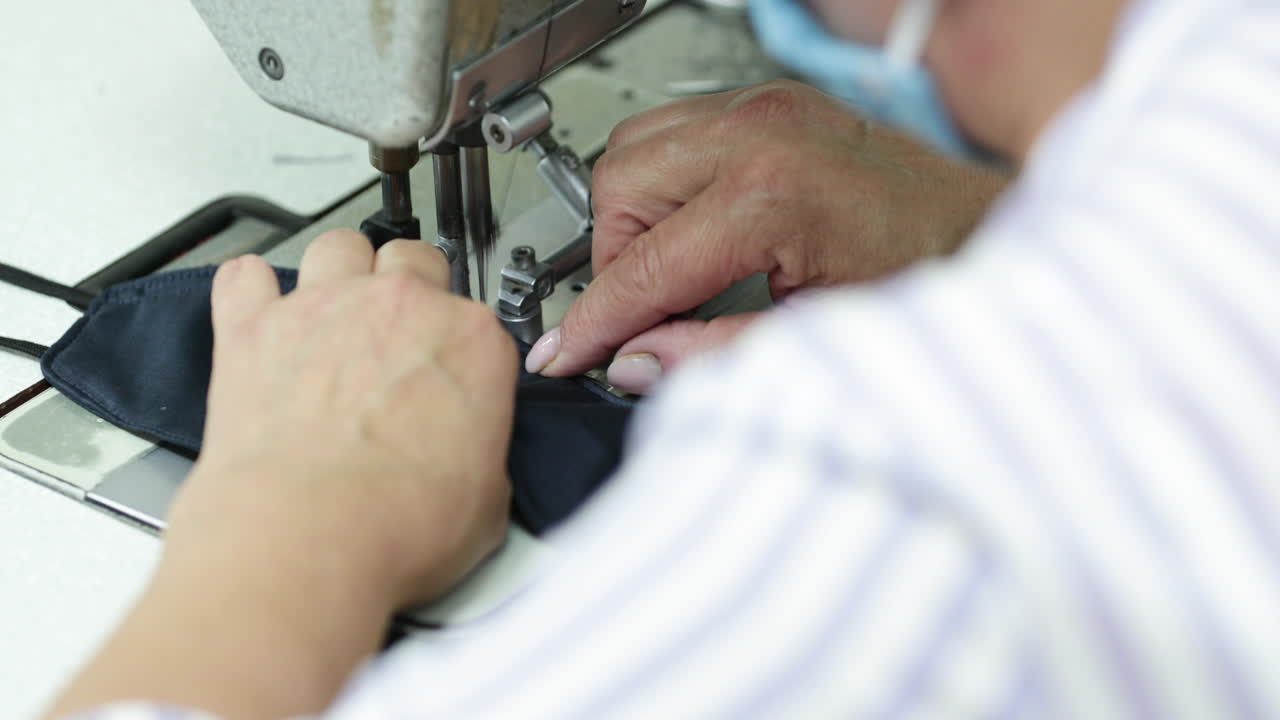 A Sew Factory Seamstress Stitching Vertically The Folded Edges Of The Blue Face Mask - Covid-19 Pandemic - Closeup Shot Pan Left