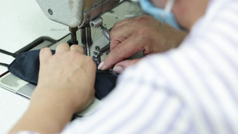 a sew factory seamstress stitching vertically the folded edges of the blue face mask - covid-19 pandemic - closeup shot pan left