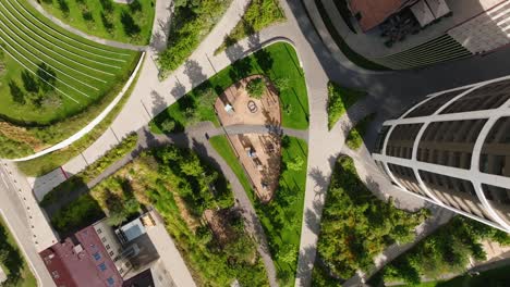 aerial top down view of kids playground, meticulously designed urban park surrounded by modern buildings, pathways, and green spaces, highlighting contemporary city planning