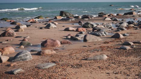 stones and pebbles cover the sandy beach as waves roll slowly in the background