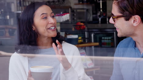 dos amigos adultos jóvenes sonriendo y hablando en una cafetería