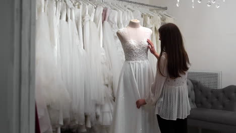 hermosa niña buscando vestido de novia en la cabina en comparación con otros vestidos. preparando para la boda. comprando un vestido de novia. la costurera inspecciona el vestido de novia hecho a medida terminado.